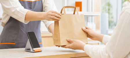 店頭スタッフがEC注文の商品が入った紙袋を顧客に手渡す様子
