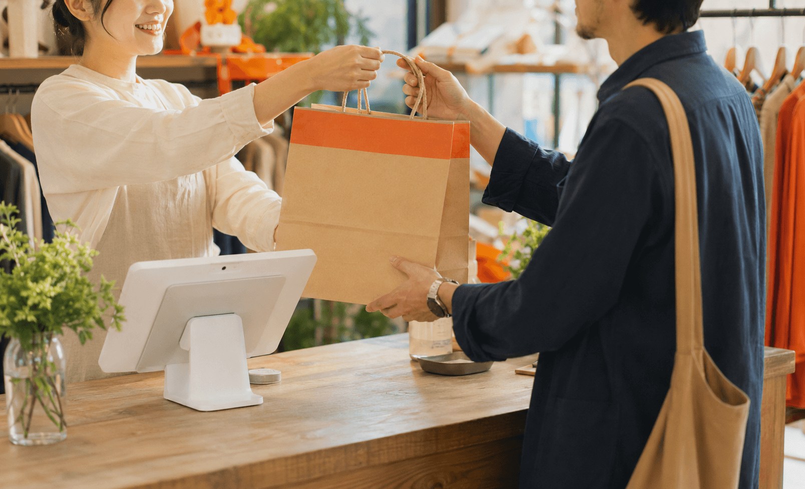 小売店のレジカウンターで買い物袋を手渡すスタッフ
