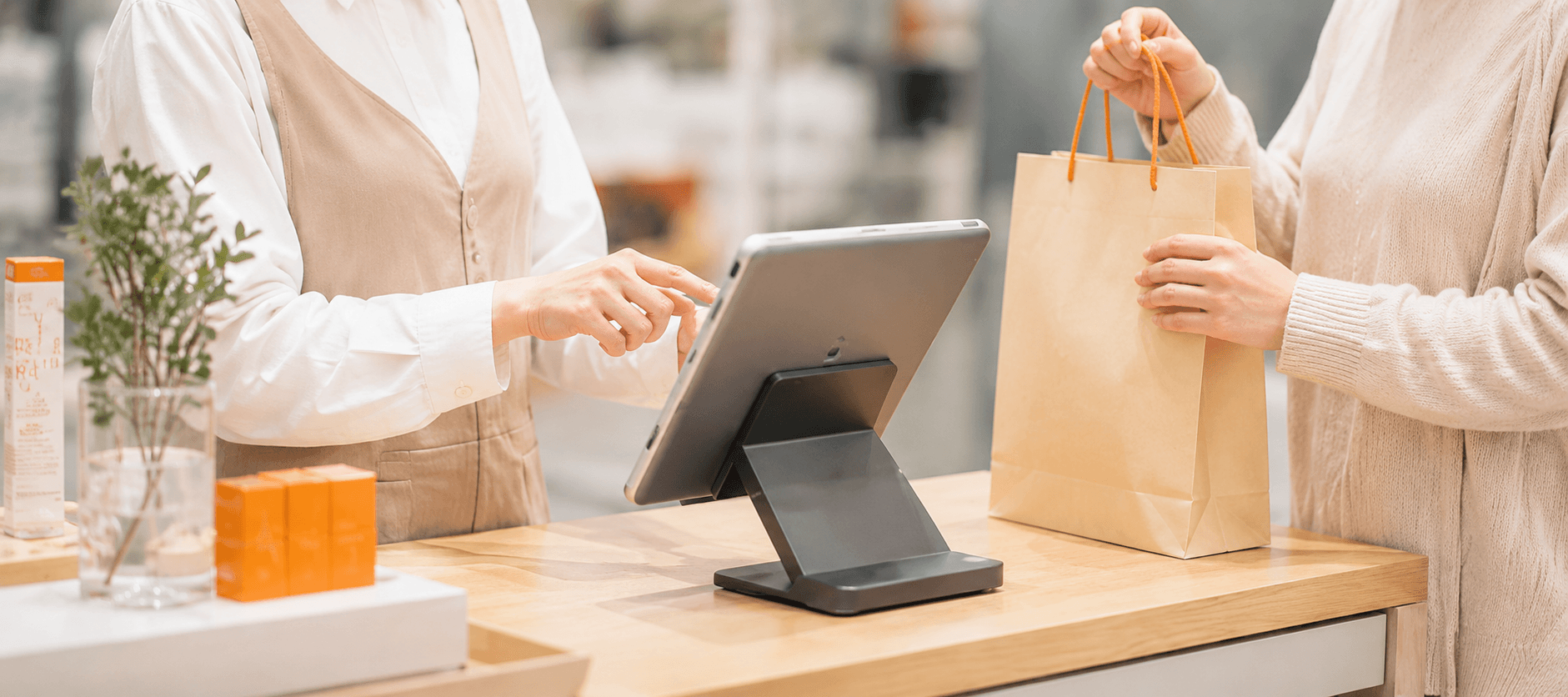 カウンターに置いたタブレットレジで会計し買い物袋を手渡す様子